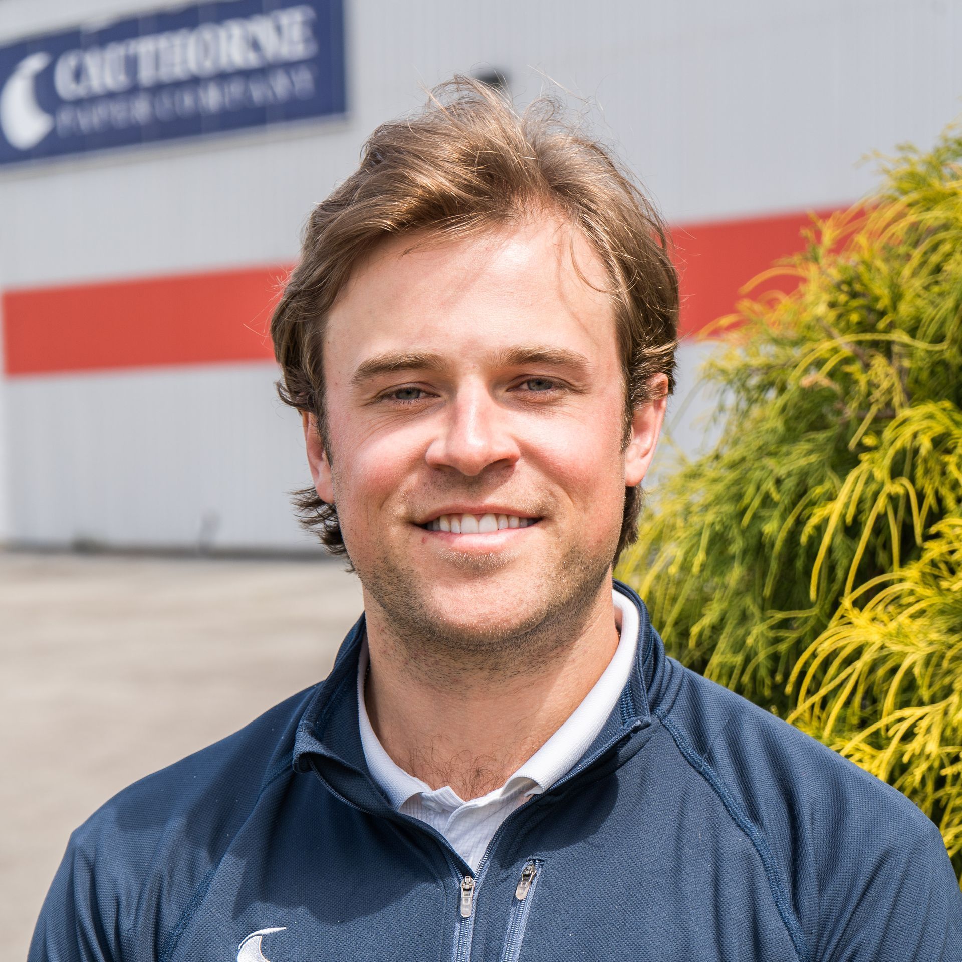 A man in a blue jacket is smiling in front of a building.