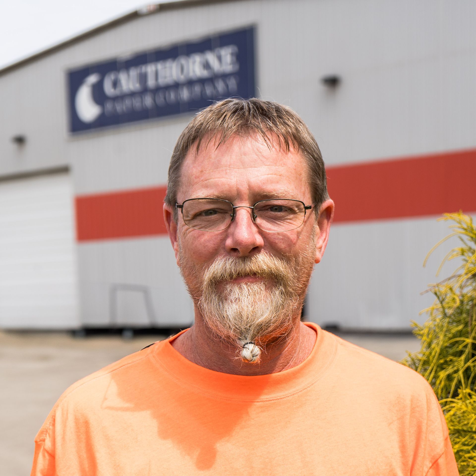 A man with glasses and a beard is standing in front of a building that says calthorne paper company