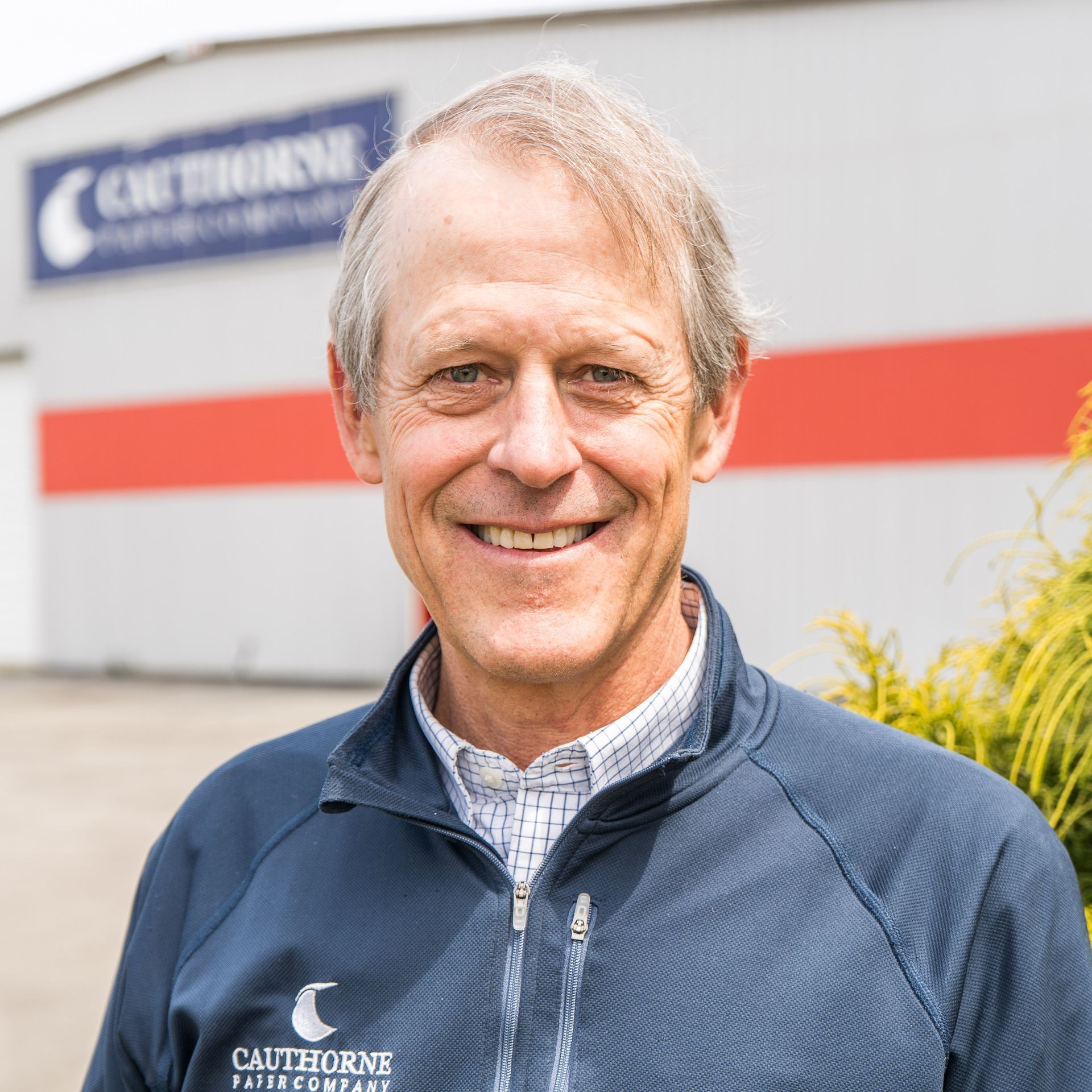 A man in a blue jacket is smiling in front of a building.