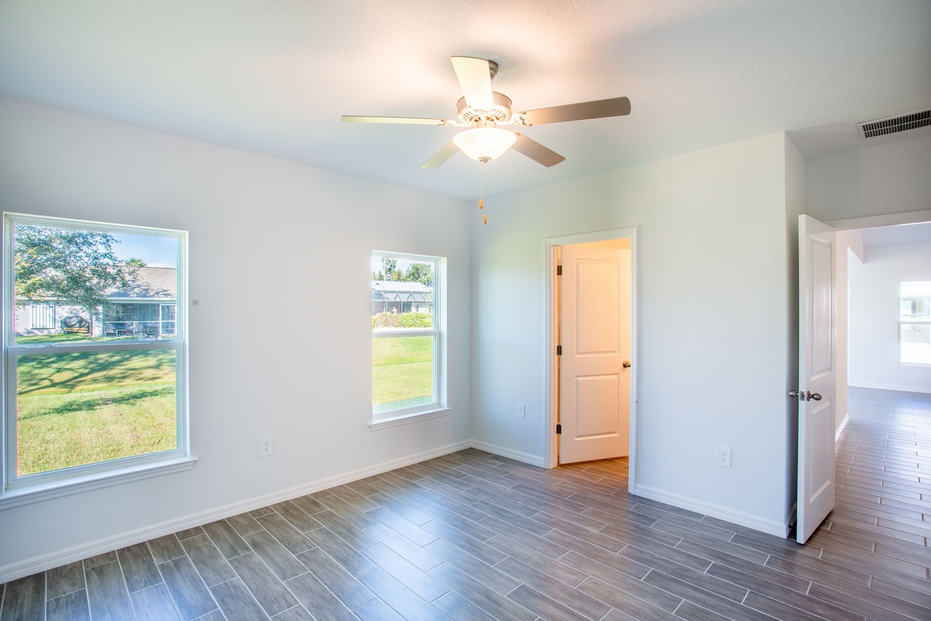 An empty bedroom with a ceiling fan and two windows.