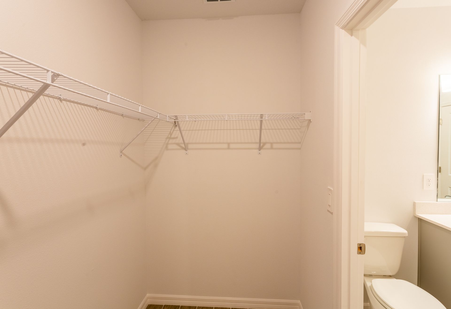 A walk in closet with shelves and a toilet in a bathroom.