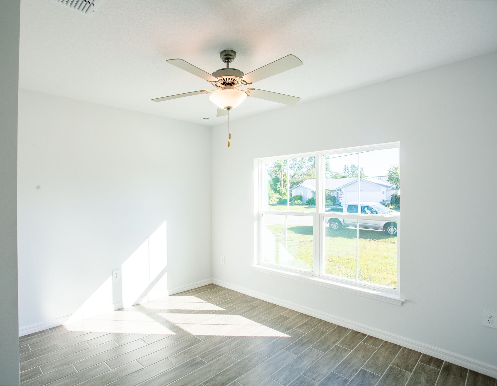 An empty room with a ceiling fan and a window.