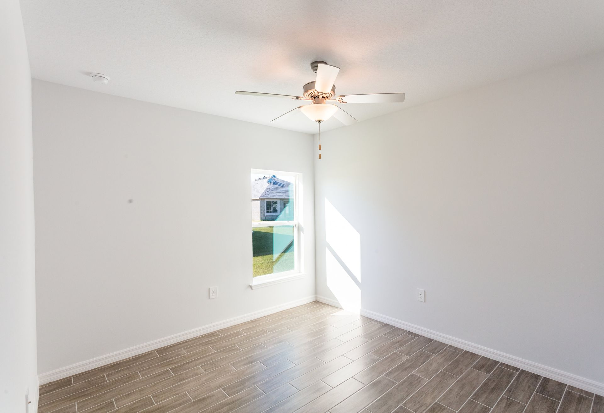 An empty bedroom with a ceiling fan and a window.