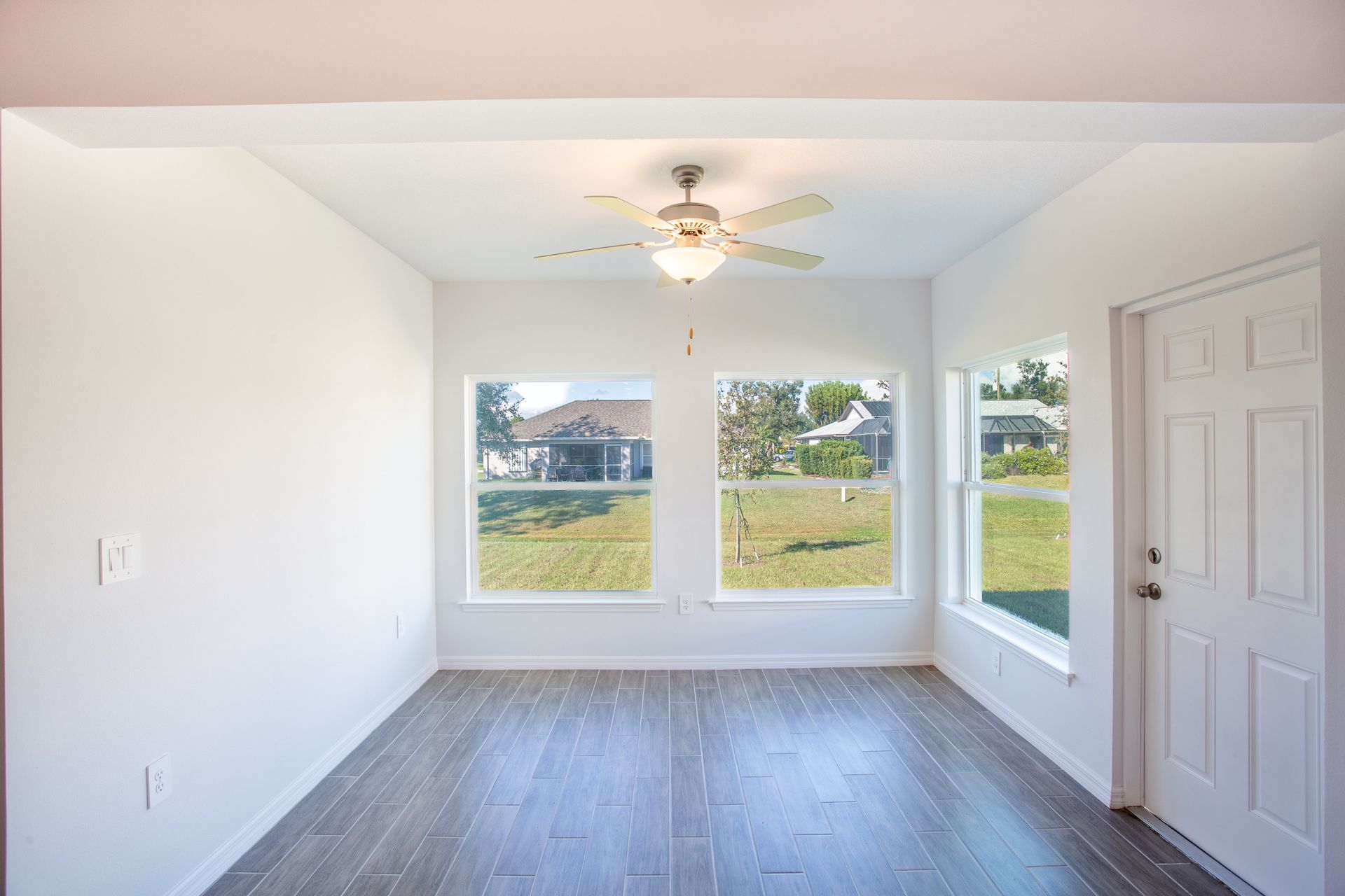 An empty room with a ceiling fan and two windows.