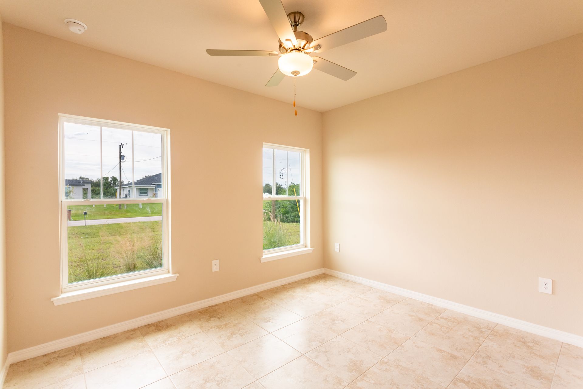 An empty bedroom with two windows and a ceiling fan.