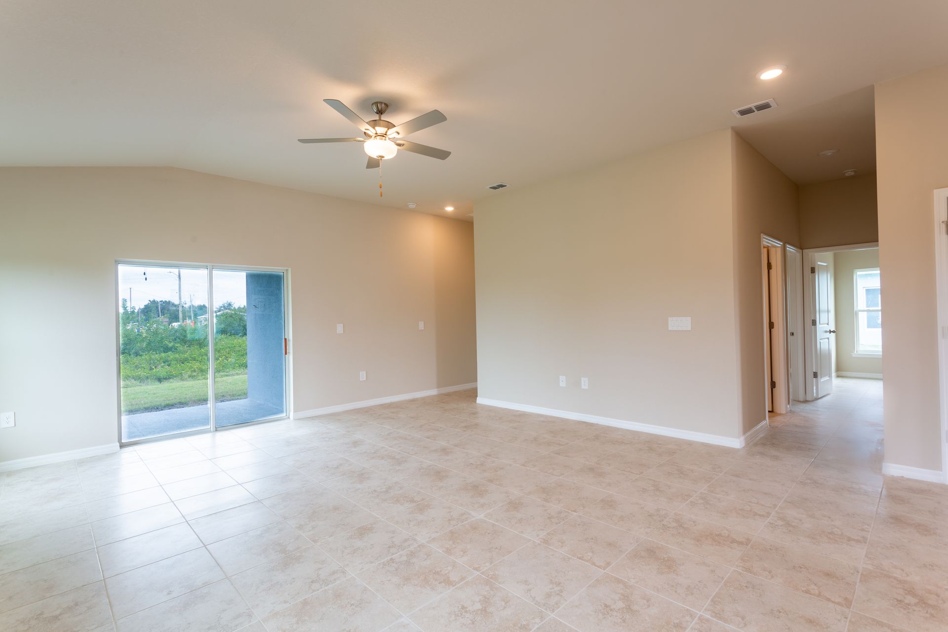 An empty living room with a ceiling fan and sliding glass doors.