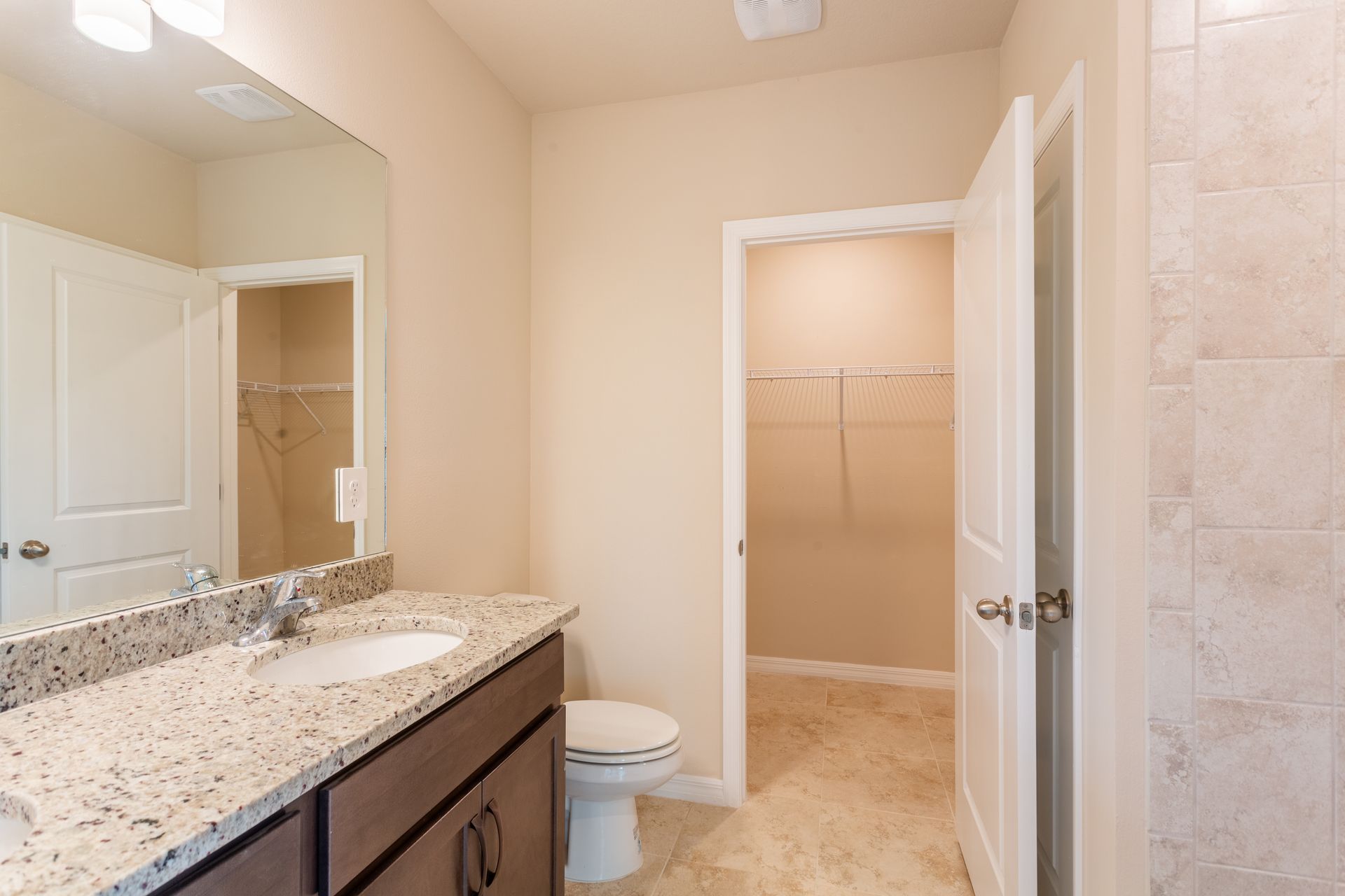 A bathroom with a toilet , sink , mirror and walk in closet.