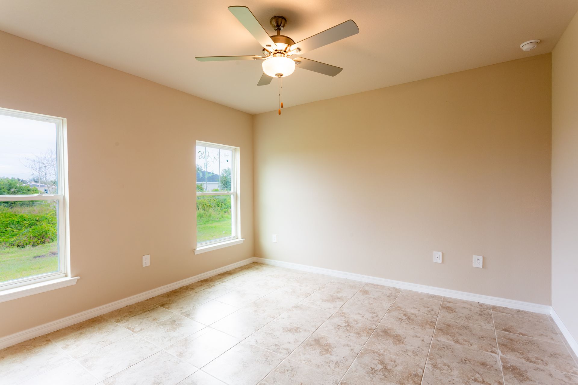 An empty bedroom with a ceiling fan and two windows.