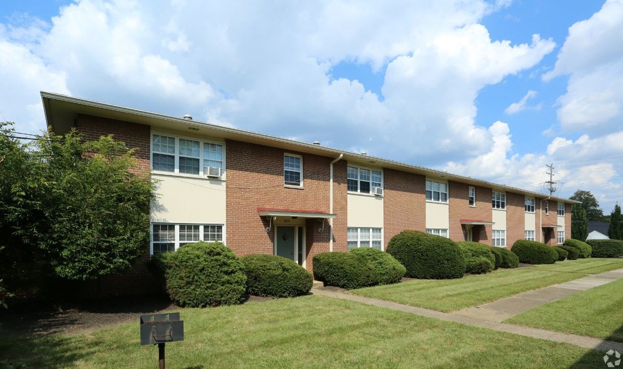 A brick apartment building with a lot of windows and bushes in front of it.