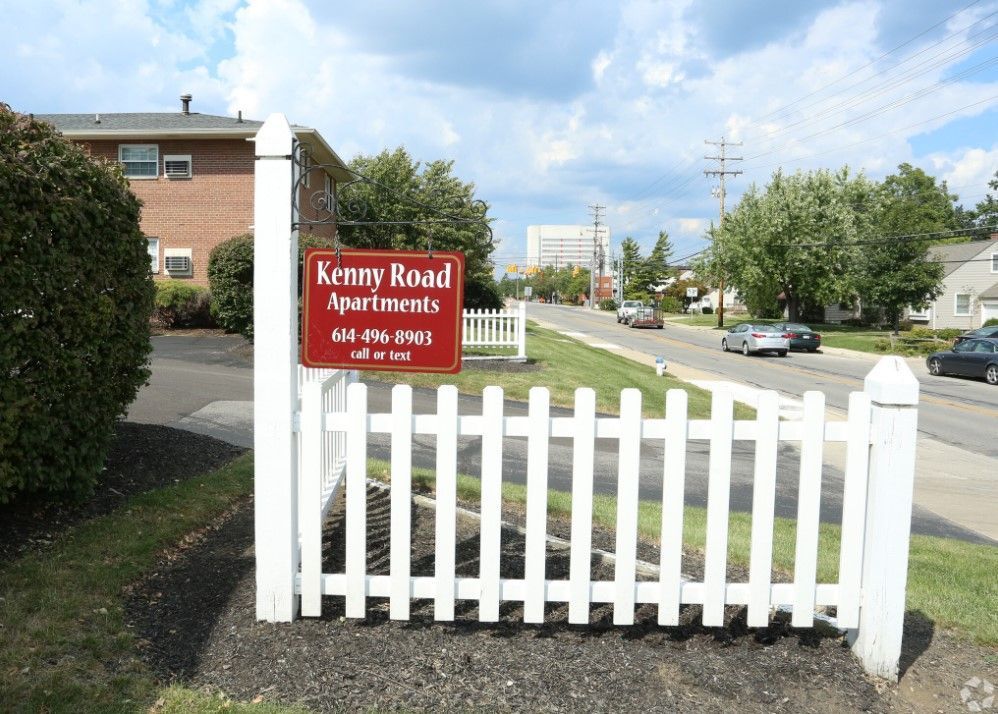 A sign for kenny road apartments is behind a white picket fence