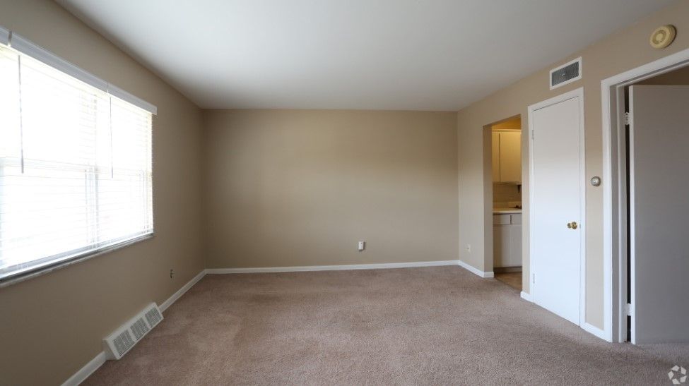 An empty living room with a carpeted floor and a window.