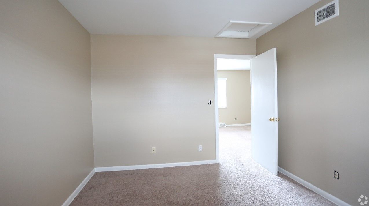 An empty bedroom with a door open and a carpeted floor.
