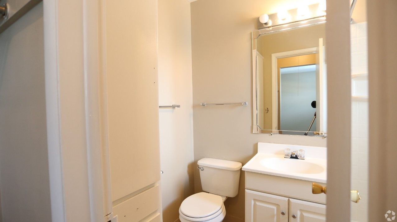 A bathroom with a toilet , sink and mirror.