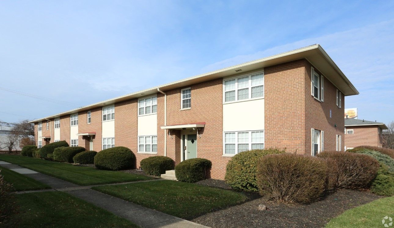 A brick apartment building with a lot of windows and bushes in front of it.