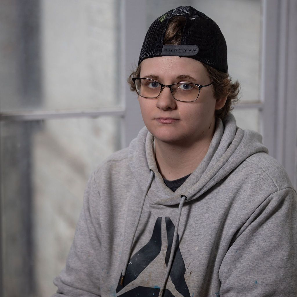 Person wearing glasses, a baseball cap, and a gray hoodie, looking at the camera.