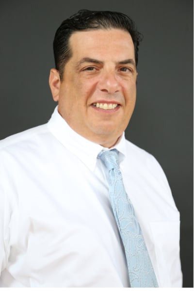 A man in a white shirt and blue tie is smiling for the camera.
