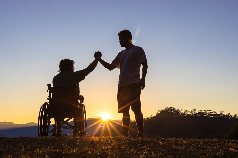 A man in a wheelchair is giving a high five to another man.