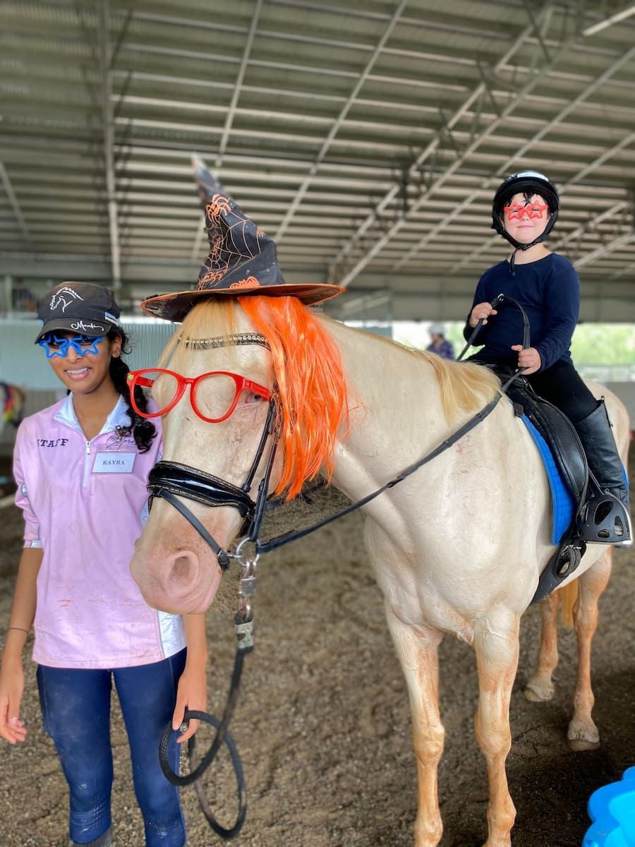 A Girl is Standing Next to a Horse Wearing a Witch Hat and Glasses — Meraki Equestrian Centre in Mareeba, QLD