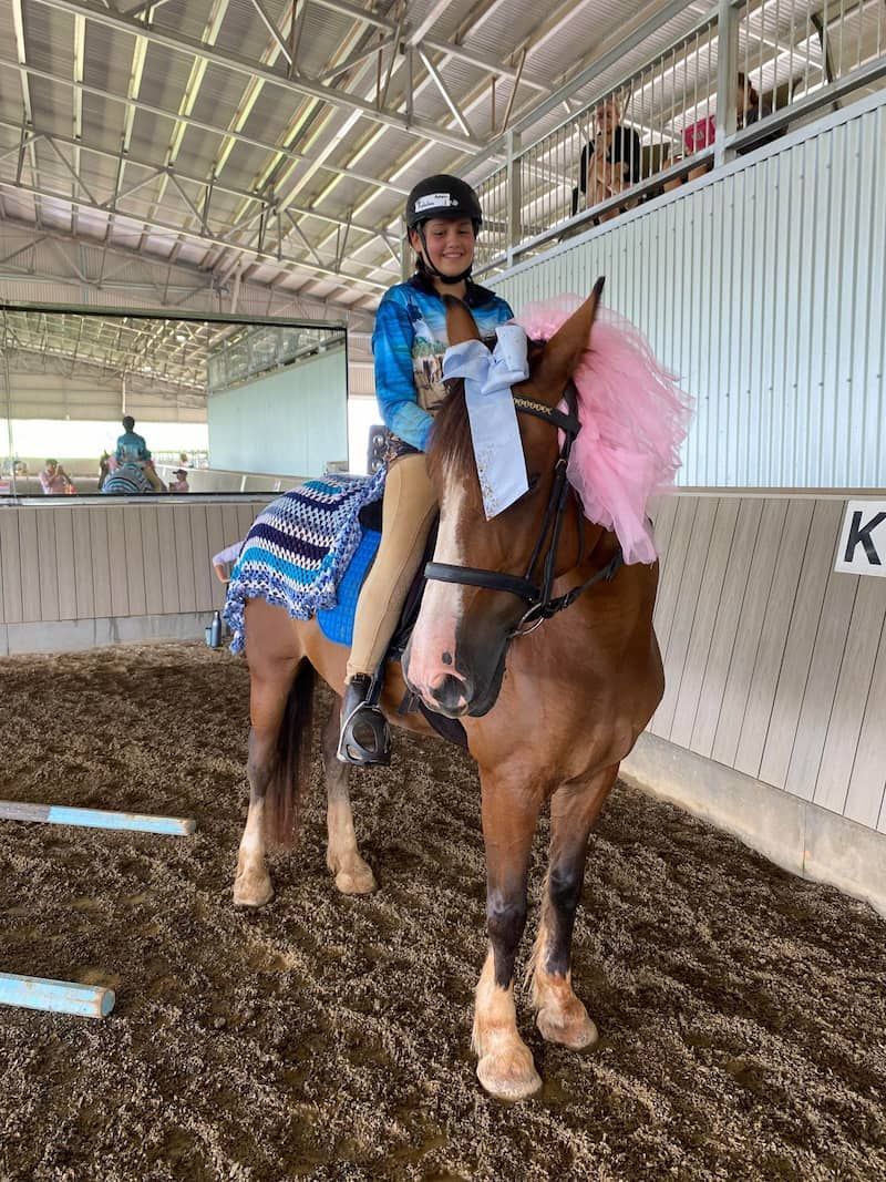 A Young Girl is Riding a Brown Horse in an Indoor Arena — Meraki Equestrian Centre in Mareeba, QLD