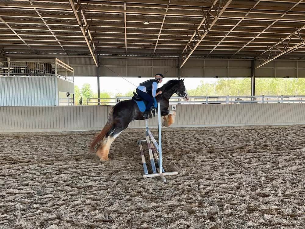 A Man is Riding a Horse Over a Jump in an Indoor Arena — Meraki Equestrian Centre in Mareeba, QLD