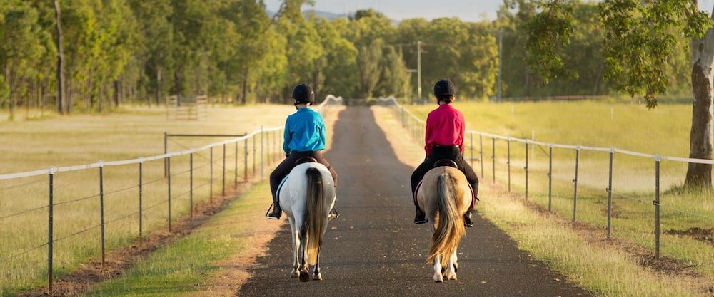 Two People Are Riding Horses Down a Dirt Road — Meraki Equestrian Centre in Mareeba, QLD