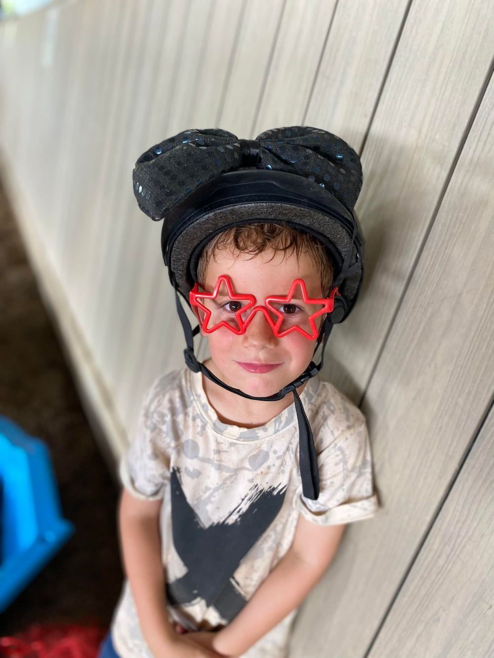A Young Boy Wearing a Helmet and Sunglasses is Standing in Front of a Wooden Wall — Meraki Equestrian Centre in Mareeba, QLD