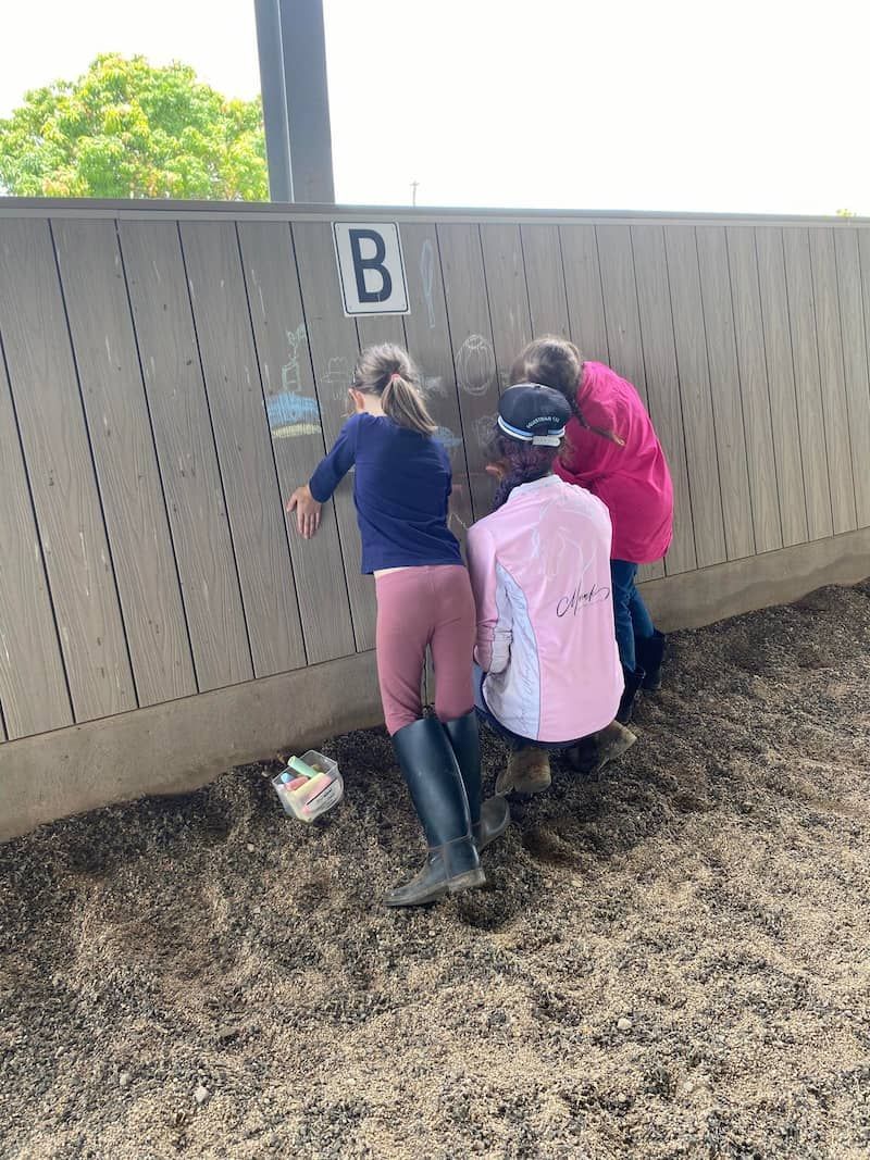 Two Young Girls Are Hugging Each Other in Front of a Wooden Fence — Meraki Equestrian Centre in Mareeba, QLD