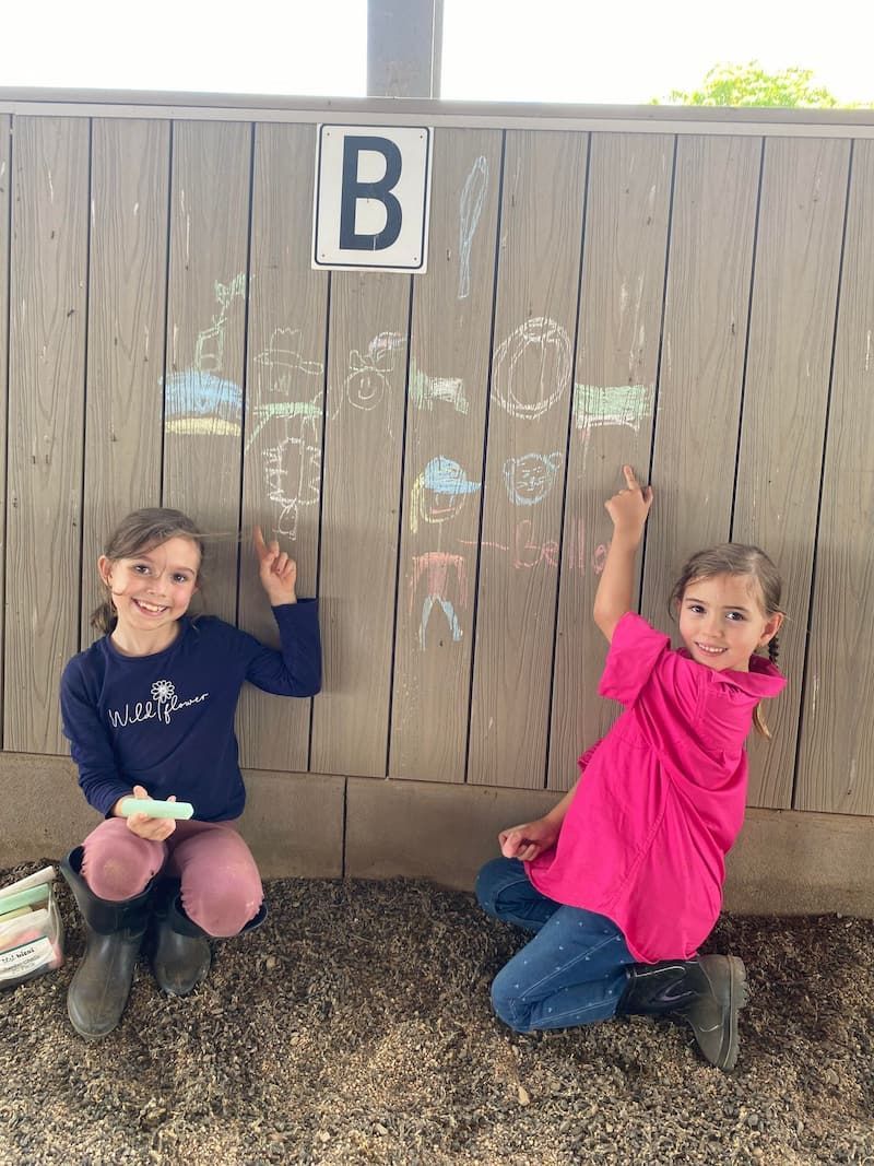 Two Young Girls Are Kneeling in Front of a Wooden Fence — Meraki Equestrian Centre in Mareeba, QLD