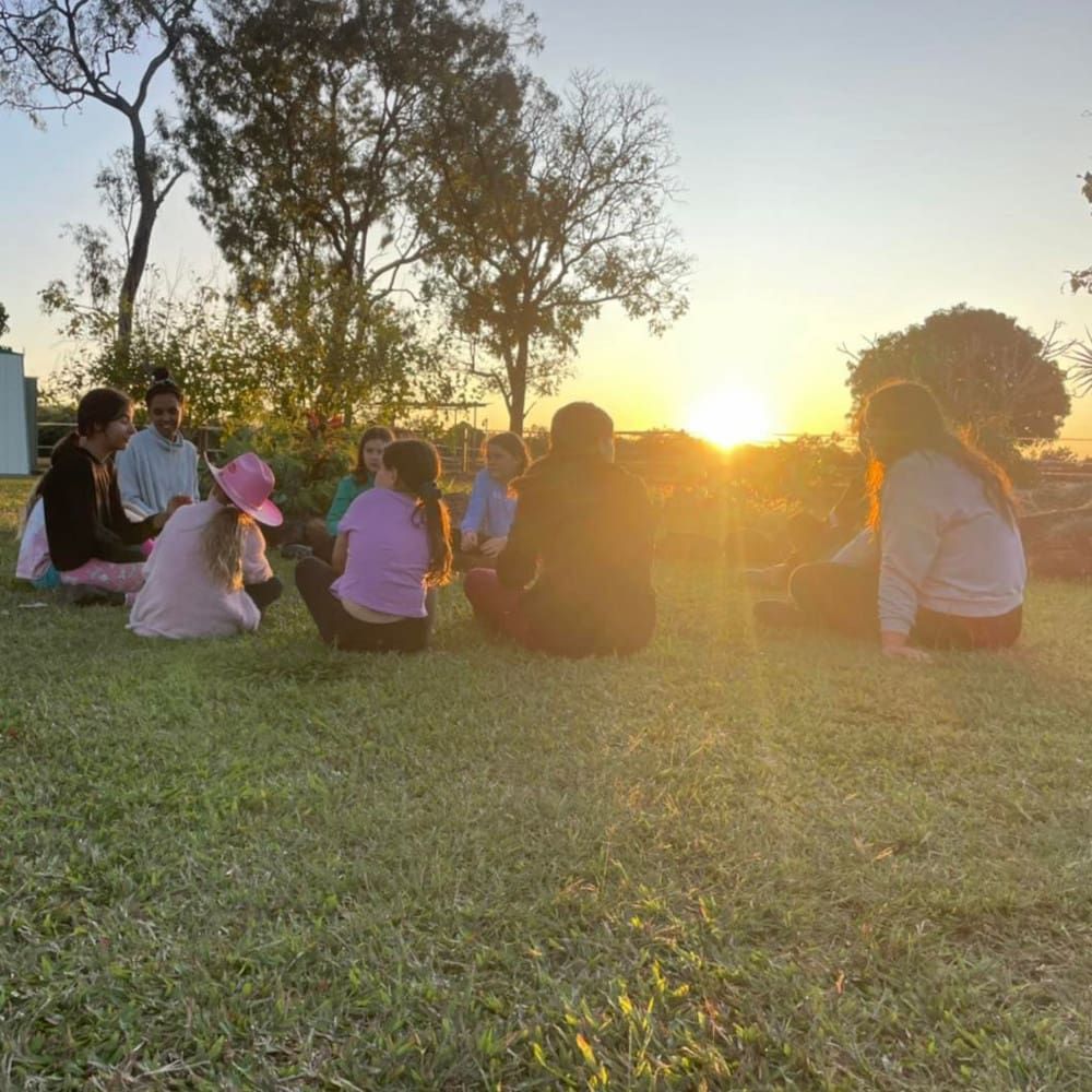 A Group of People Are Sitting in a Circle on the Grass at Sunset — Meraki Equestrian Centre in Mareeba, QLD