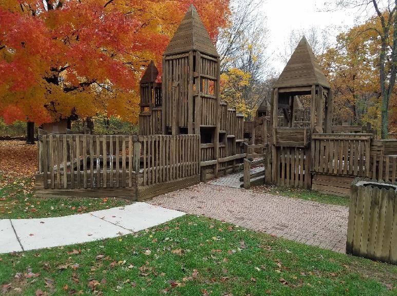 A wooden playground in a park with trees in the background.