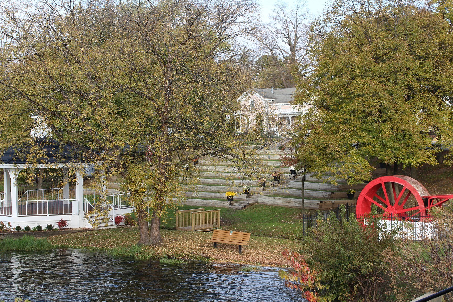 A large red wheel is in the middle of a park next to a pond.