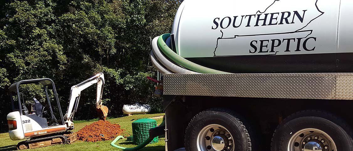 A Southern Septic truck parked on grass near an excavator digging a hole in the ground.