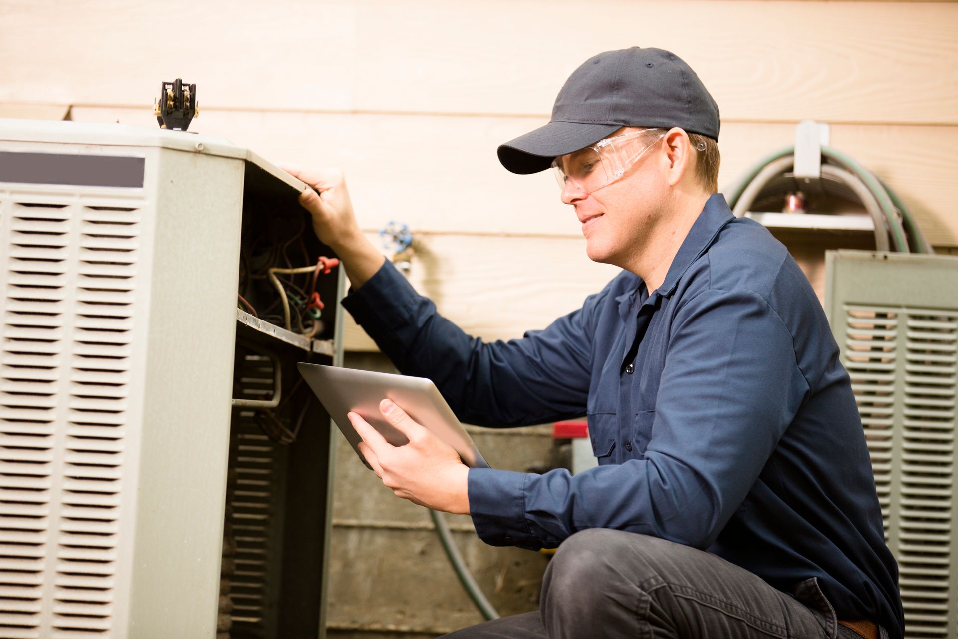 A person wearing goggles and a cap fixing an AC