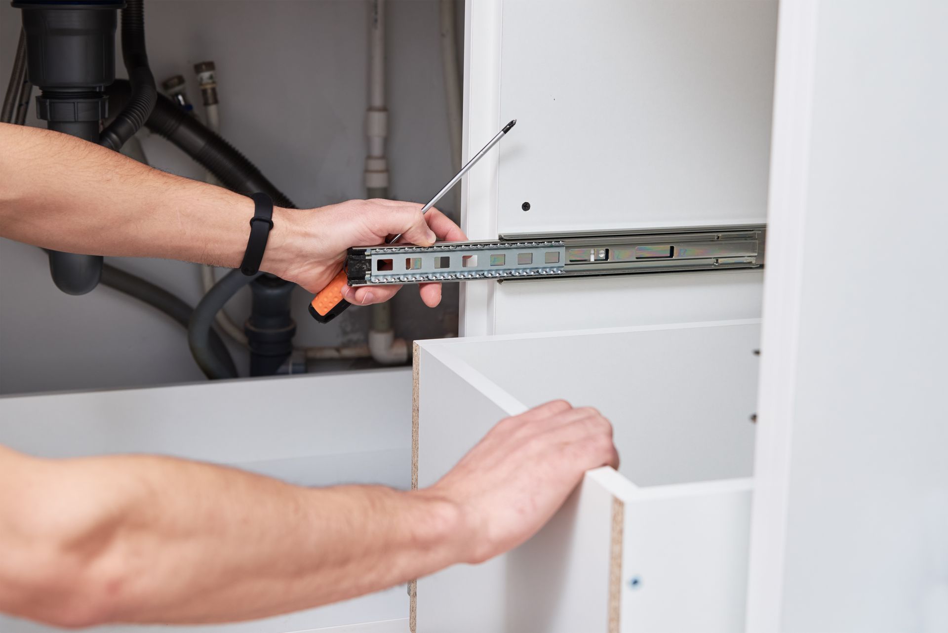 A male carpenter is seen diligently repairing and installing a shelf inside a kitchen cabinet.