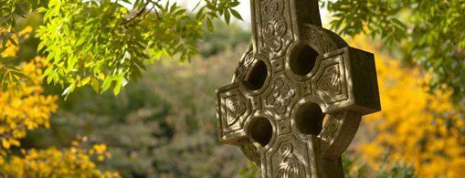 A Celtic-cross memorial beneath trees in autumn