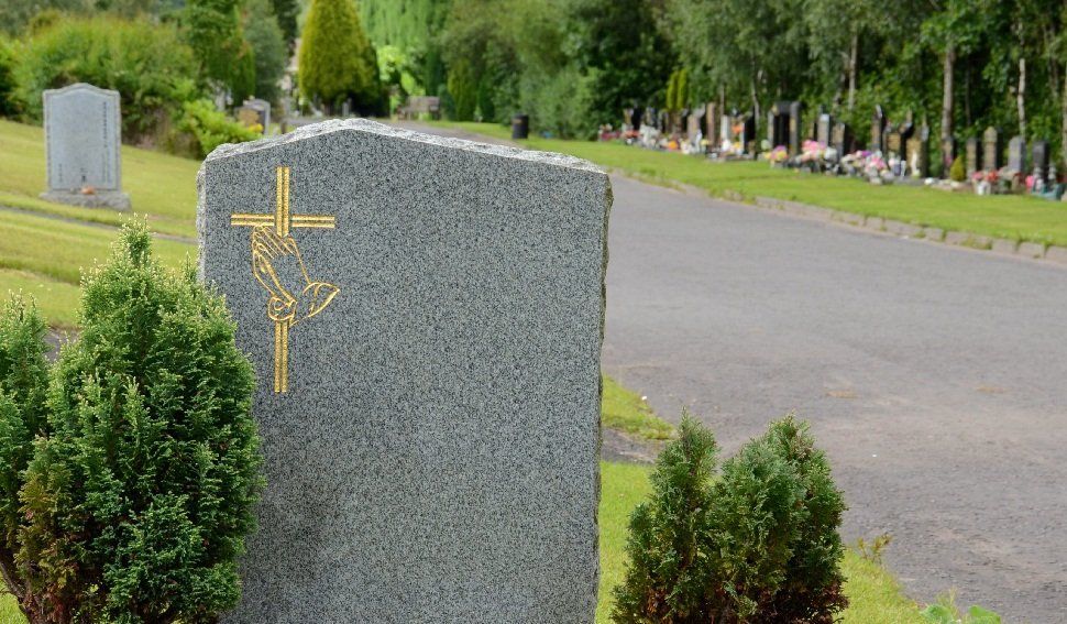 A gravestone with a gold cross and praying-hands carving, in a cemetry