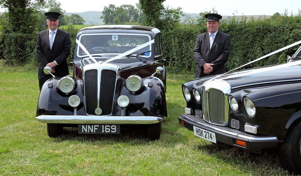 Two chauffeurs next to classic wedding cars