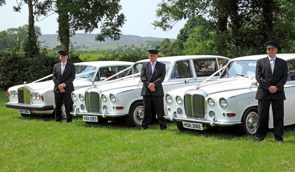 Three chauffeurs beside three white wedding cars