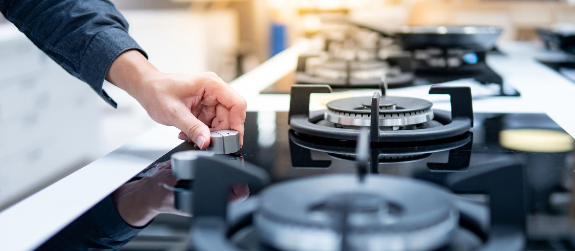 Person turning a stove knob on a black stovetop.