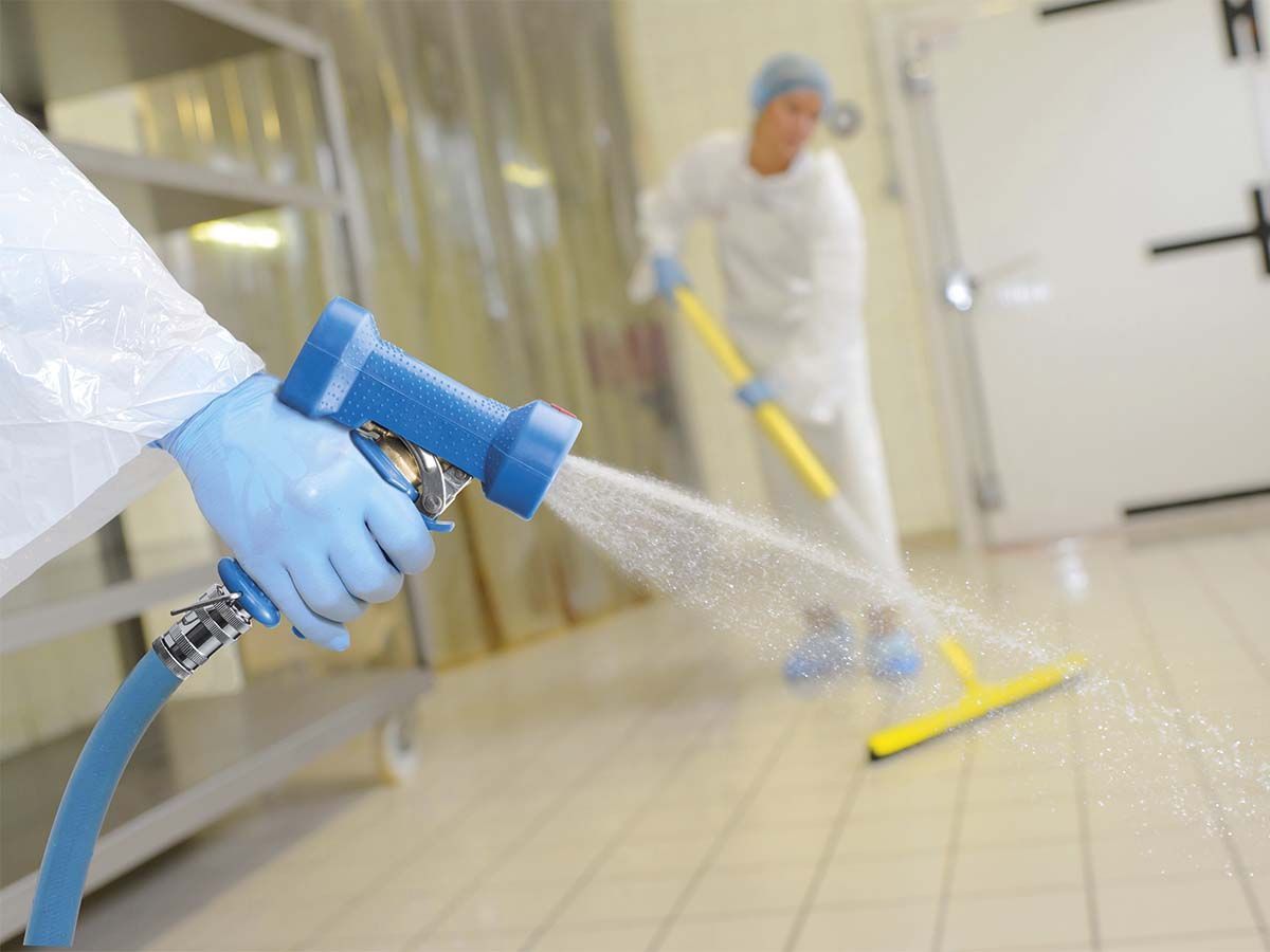 A person wearing blue gloves is spraying water on a tiled floor