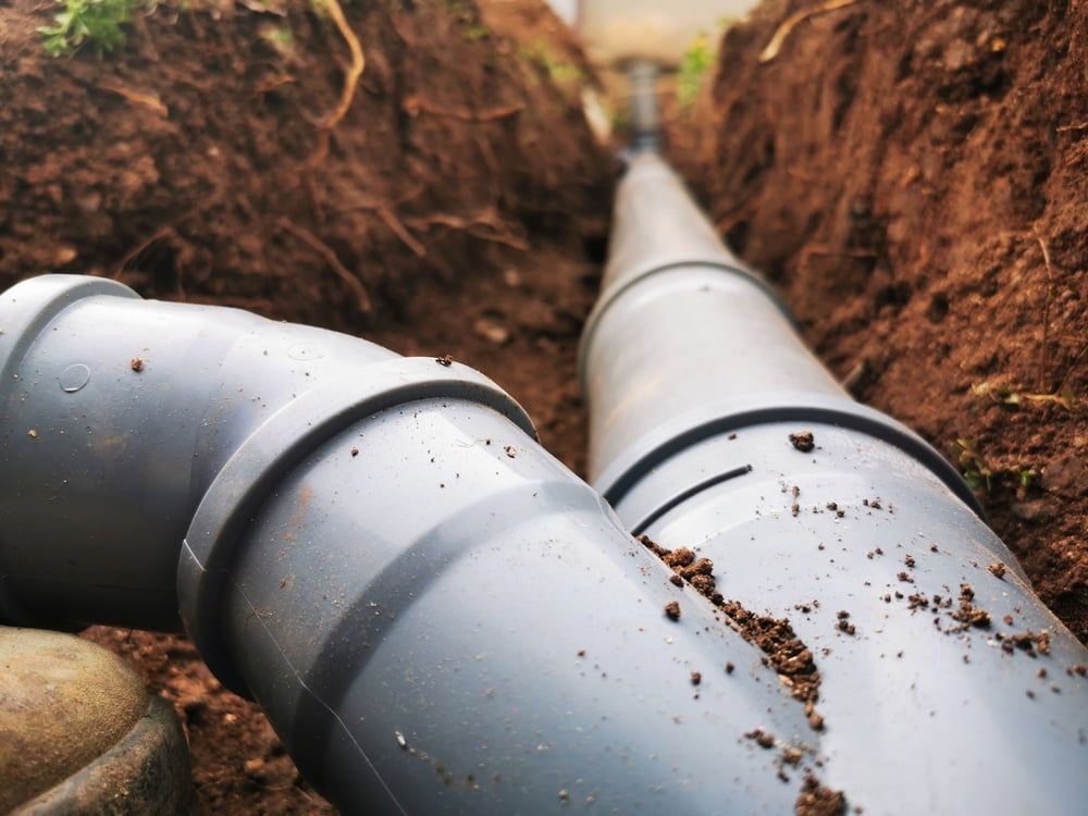 Grey Underground Pipes in a Trench, With Dirt and Rocks Along the Sides — Mark's Plumbing in Budgewoi, NSW