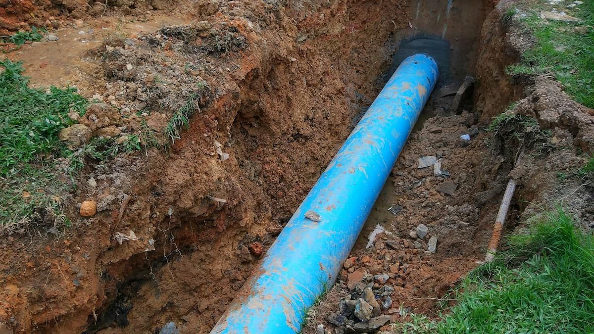 Bright Blue Pipe Laid in an Excavated Dirt Trench Beside Grass — Mark's Plumbing in Central Coast, NSW