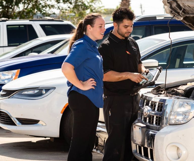 Two people inspect a white SUV in a car lot, one holding a tablet. | Dub's Garage