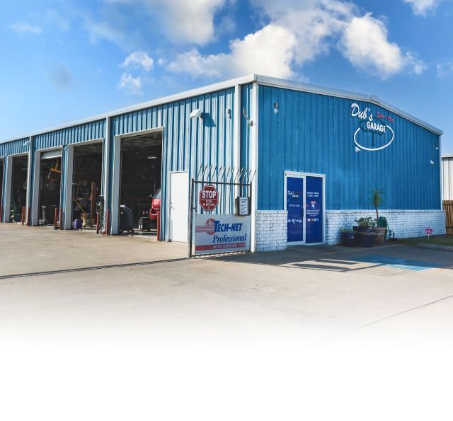 Blue auto repair shop with open service bays and white trim under a clear sky | Dub's Garage