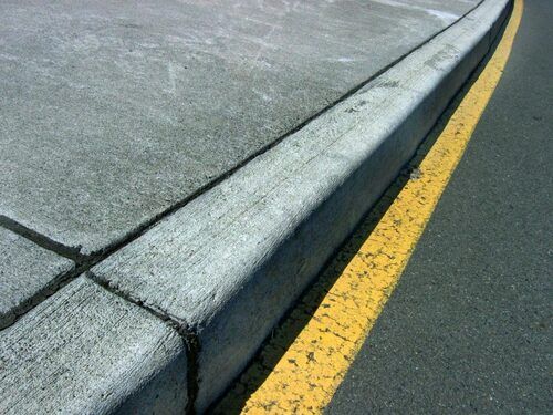 Concrete curb beside a yellow road line on gray pavement | Dub's Garage