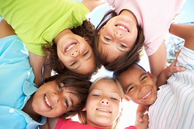 Group of smiling children looking down, arms around each other.