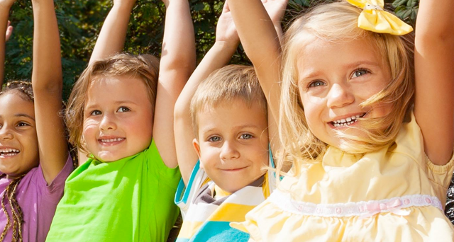 Group of smiling children looking down, arms around each other.