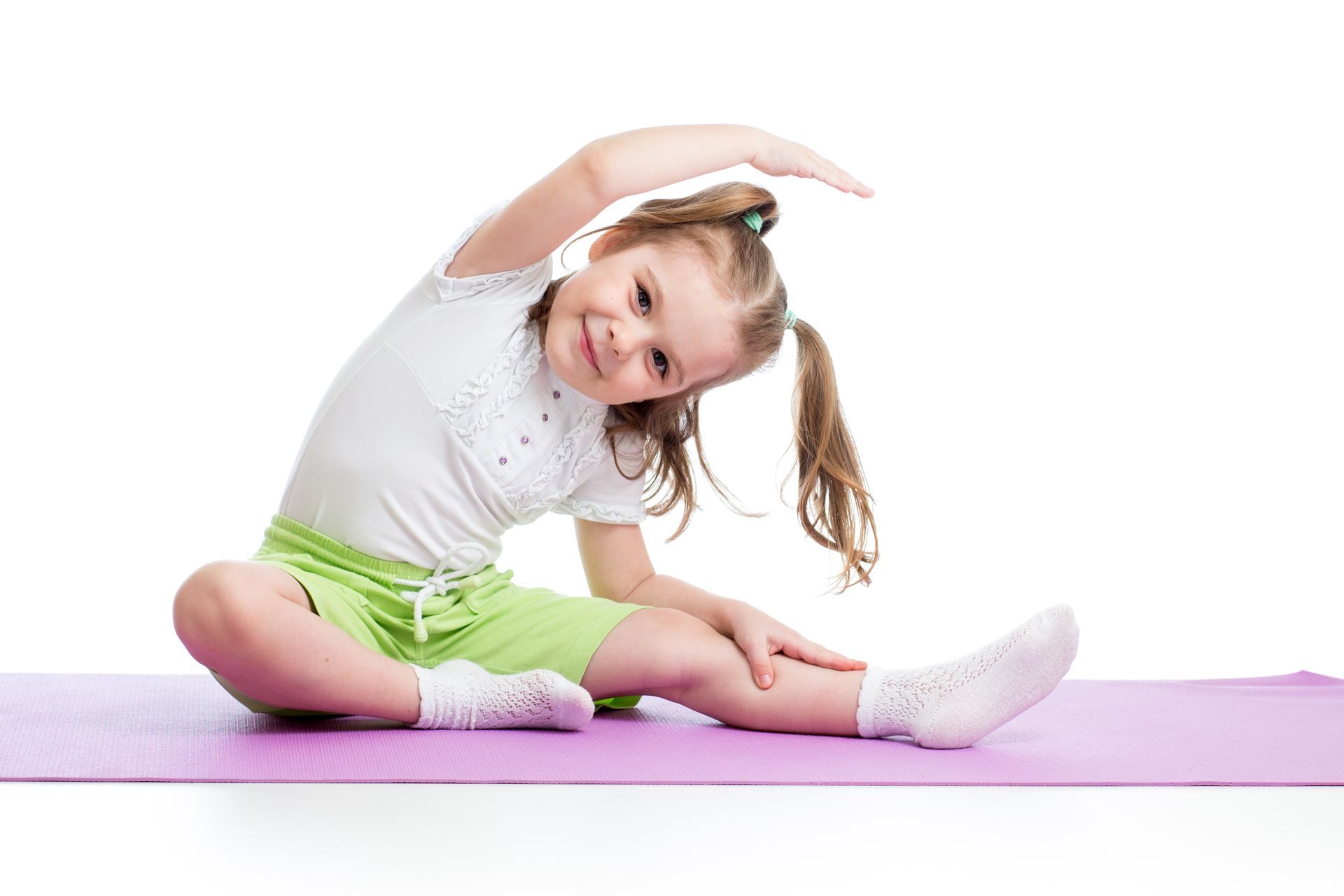 Girl in green shorts stretches on a purple mat, reaching to the side.
