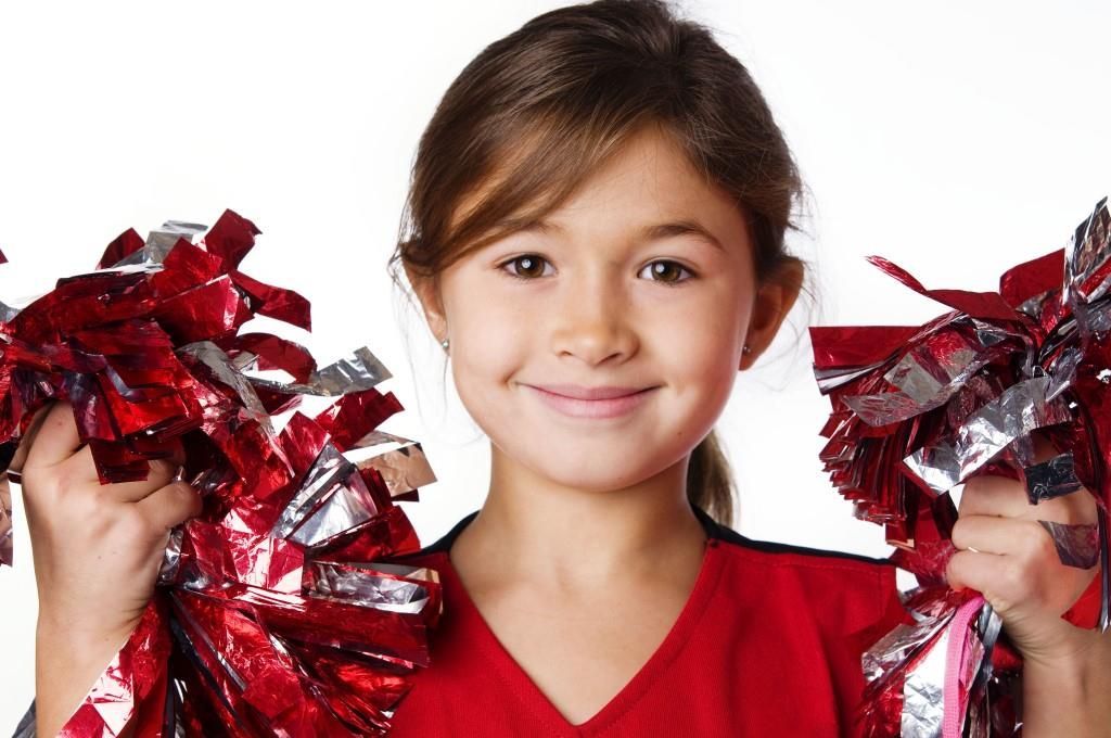 Girl in red shirt holding red and silver pom-poms, smiling.