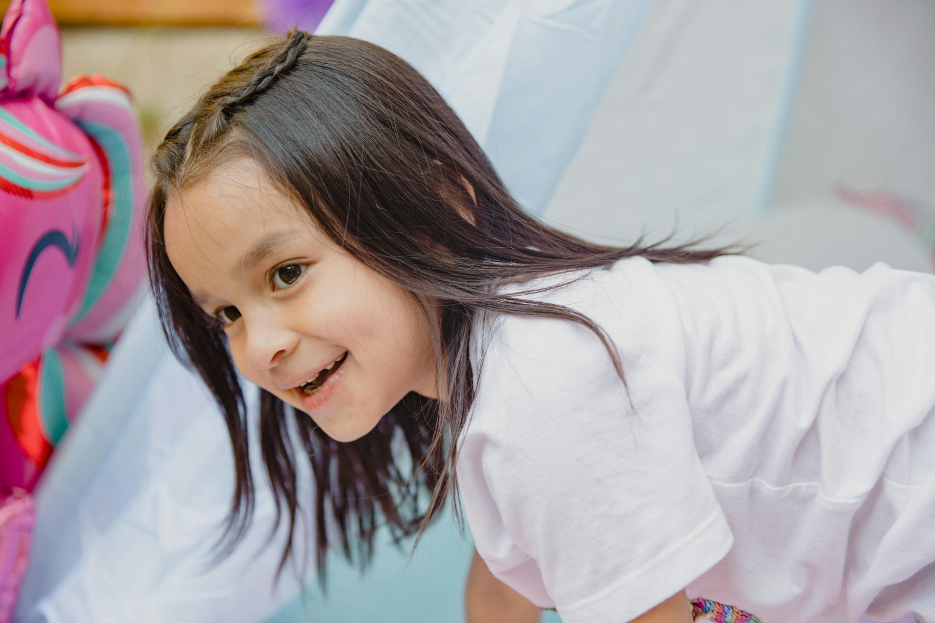 Girl with dark hair smiles, leaning over, near a My Little Pony balloon.
